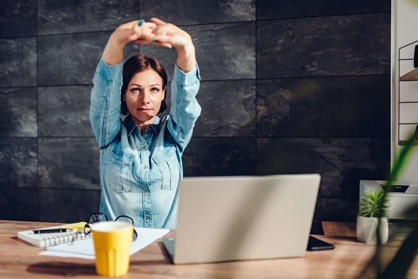 Business woman wearing denim shirt stretching arms in the office