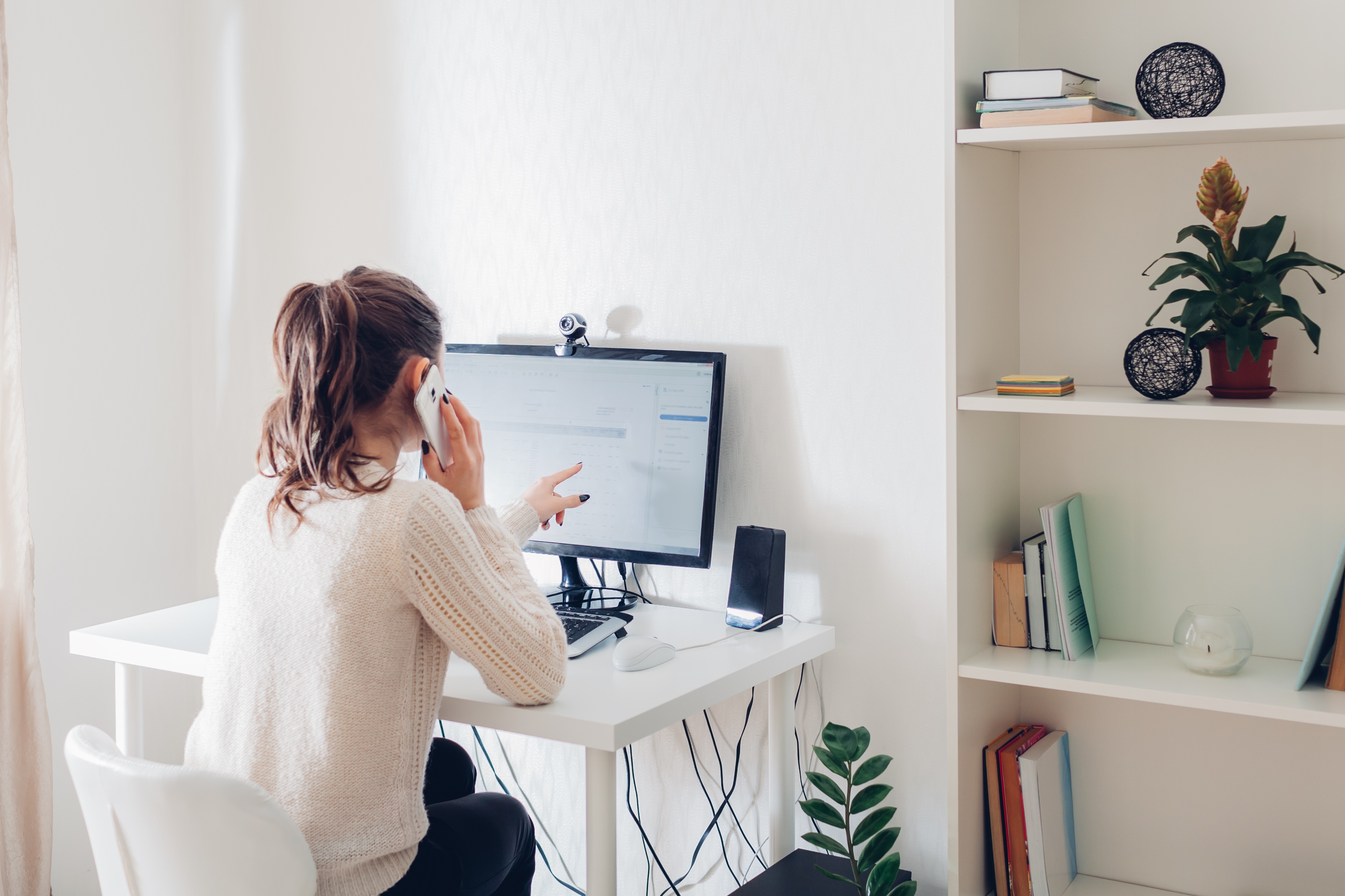 Work from home during coromavirus pandemic. Woman stays home talking on phone. Workspace of freelancer. Office interior with computer