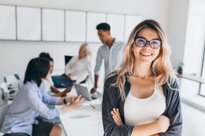 blonde female executive posing with smile arms crossed during brainstorm with managers indoor portrait european student spending time hall with asian african friends 1